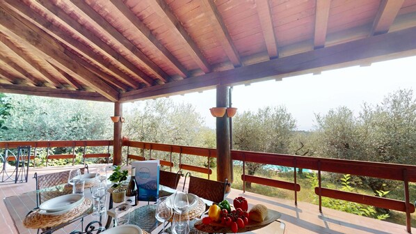 Un espace extérieur abrité, aménagé pour les repas, avec une table pour deux, entouré de rampes en bois, et offrant une vue sur un paysage arboré et sur le ciel.