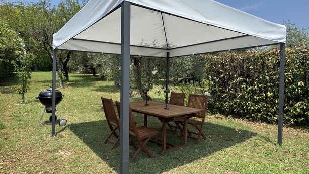 Een overdekte buitenruimte met eettafel, stoelen, een barbecue en een tentstructuur.
