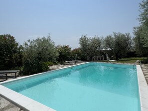 Une piscine rectangulaire dont les bords sont recouverts de carreaux, entourée de verdure et d’arbres.