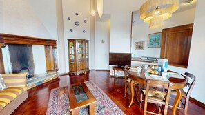 Un salon avec une cheminée, un téléviseur, une table à manger avec des chaises et un tapis à motifs.