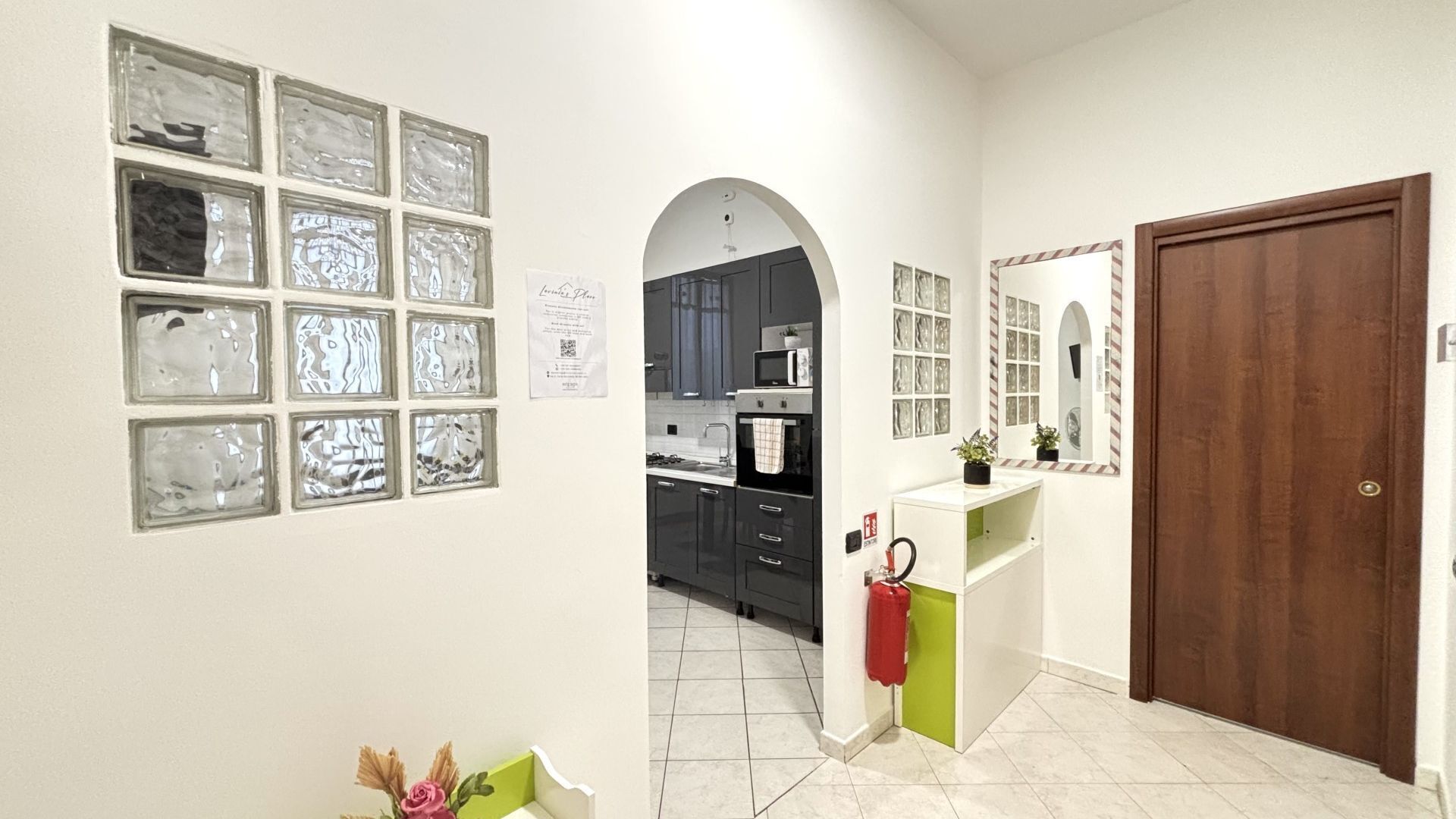 Un pasillo con una zona de cocina visible a través de un arco, una puerta y una pared con varias fotos enmarcadas.
