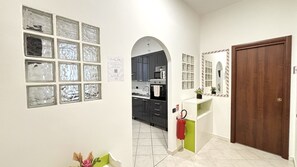 Un passadís amb una cuina visible a través d'una galeria d'arcs, una porta i una paret amb diverses fotografies emmarcades.