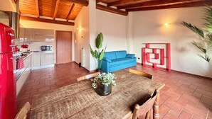 Ein großzügiger Wohnbereich mit Holzboden, einem blauen Sofa, einem Esstisch mit Stühlen und einem roten Wandelement.