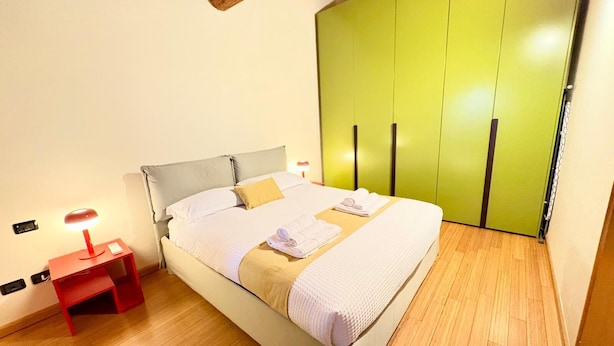 Ein Schlafzimmer mit einem Bett, einem Nachttisch, einer Lampe und einem grünen Kleiderschrank.