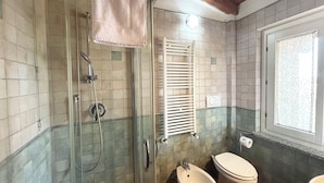 Ein Badezimmer mit einer gläsernen Duschkabine, einem Bidet, einer Toilette und einem Fenster mit Blick.