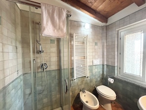 Ein Badezimmer mit einer gläsernen Duschkabine, einem Bidet, einer Toilette und einem Fenster mit Blick.
