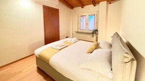 Ein Schlafzimmer mit Holzboden, einem Bett mit weißer und gelber Bettdecke, einem Fenster mit Jalousien und einem Heizkörper unter dem Fenster.