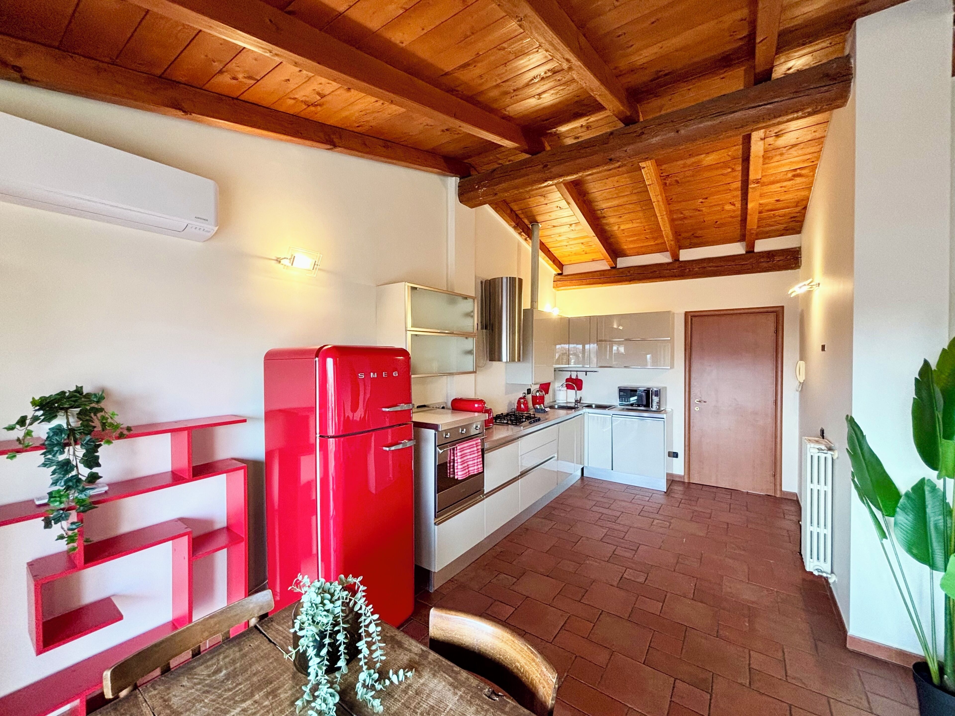 Une cuisine avec un réfrigérateur rouge, des poutres en bois au plafond et un sol carrelé.