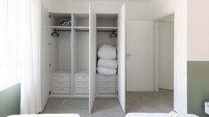 Armadio a muro con ante aperte, dotato di numerose mensole, un'asta appendiabiti e una pila di coperte piegate.