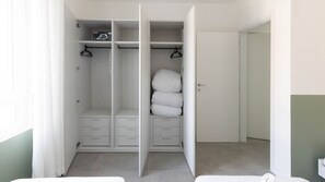 Un armari ampli amb portes obertes, amb diverses prestatgeries, una barra penjant i una pila de llençols doblegats.