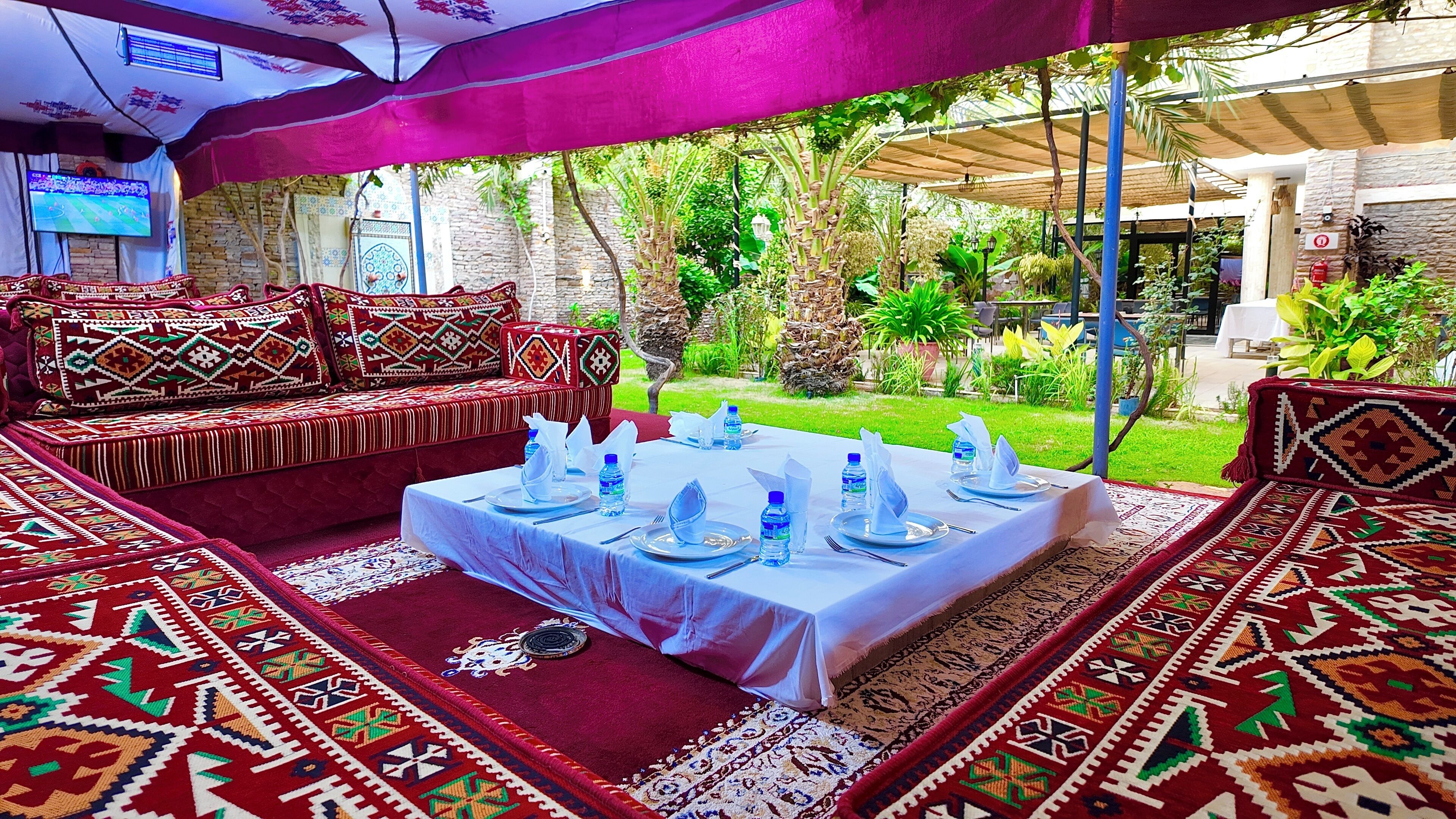 Un espacio al aire libre con mesas dispuestas para comer, rodeado de alfombras estampadas y cojines.