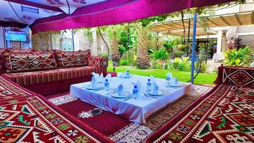Un espacio al aire libre con mesas dispuestas para comer, rodeado de alfombras estampadas y cojines.
