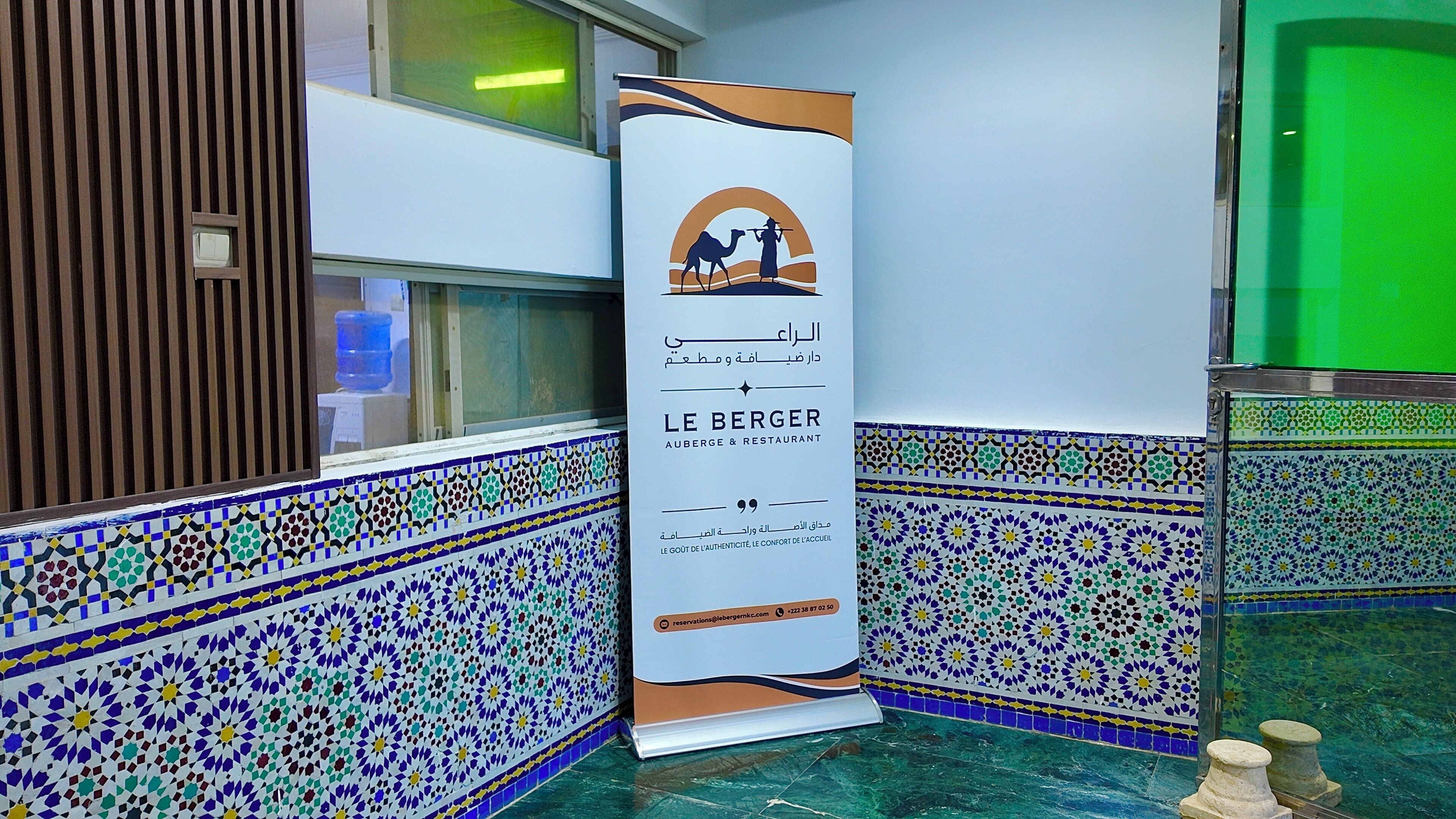 Un banner vertical amb una escena de paisatge desertàric i text, col·locat en un passadís amb terra de rajoles estampades.