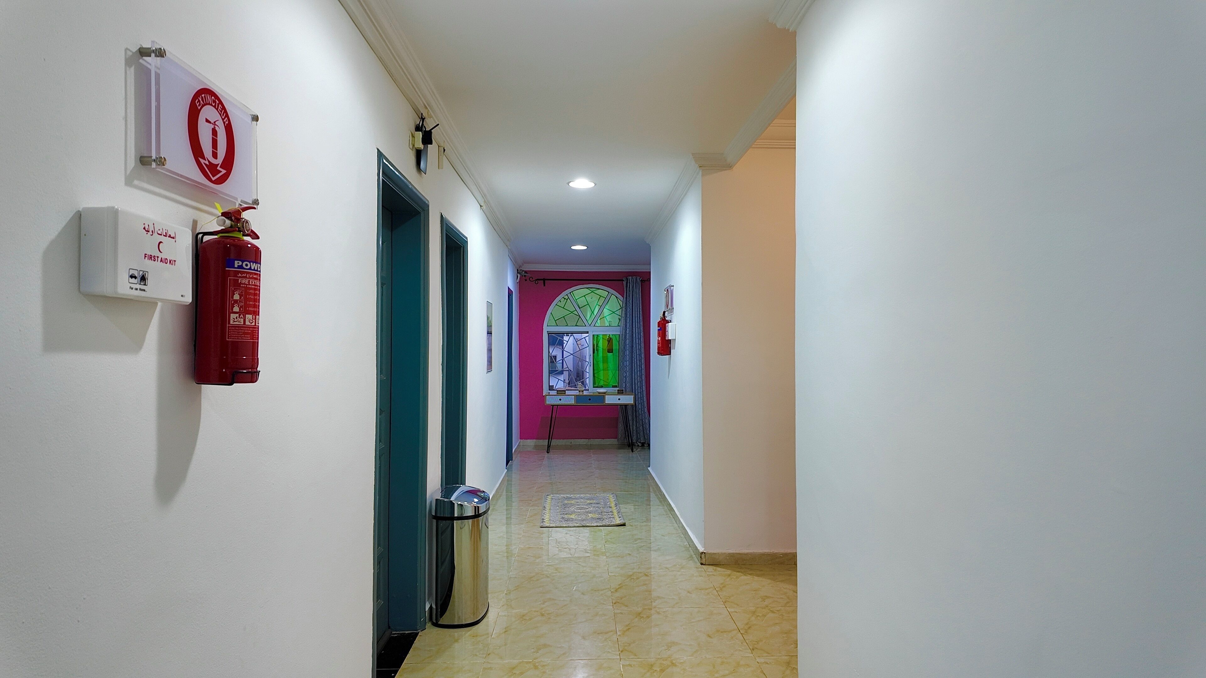 A hallway with a fire extinguisher, first aid kit, and a trash bin.