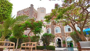 A courtyard with a stone building, benches, and trees. - Hôtel Résidence le Berger (Nouakchott)