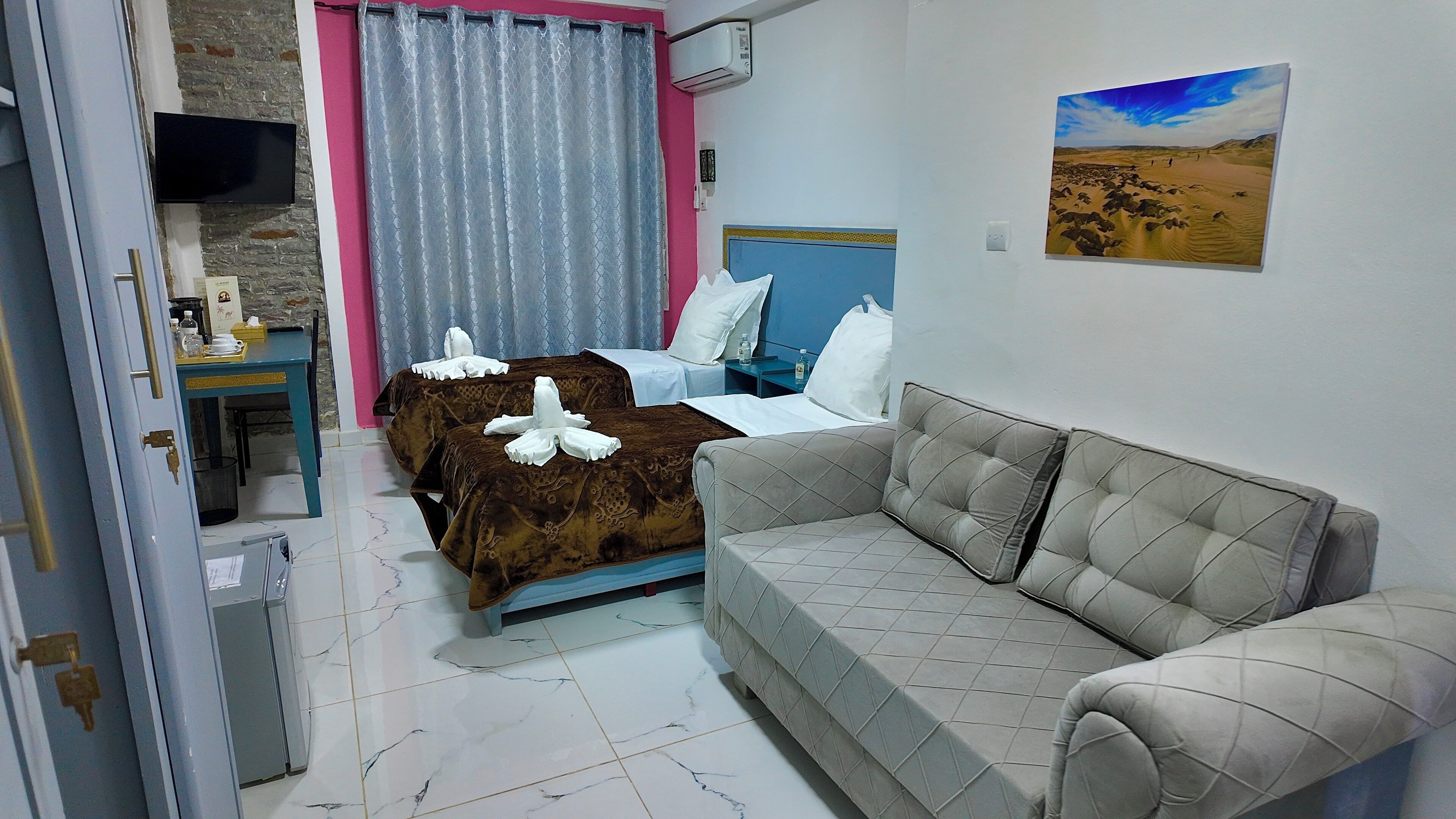 Habitació d'hotel amb un llit, un sofà, una televisió, un aparell d'aire condicionat i un quadre a la paret.