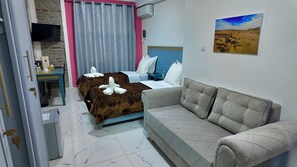 Habitación de hotel con cama, sofá, televisor, aire acondicionado y un cuadro en la pared.