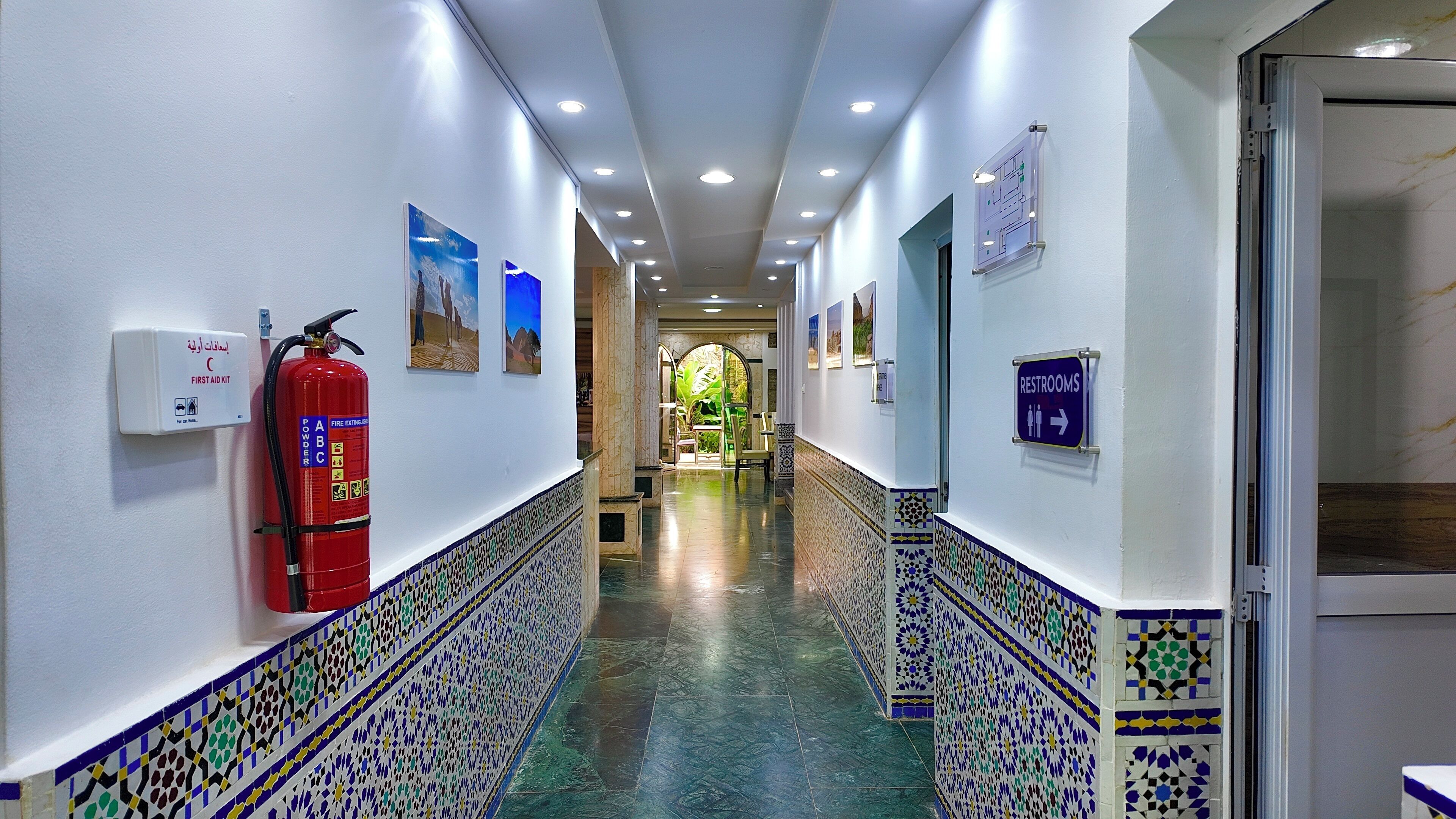 A corridor with a fire extinguisher, a first aid kit, and a sign indicating restrooms.
