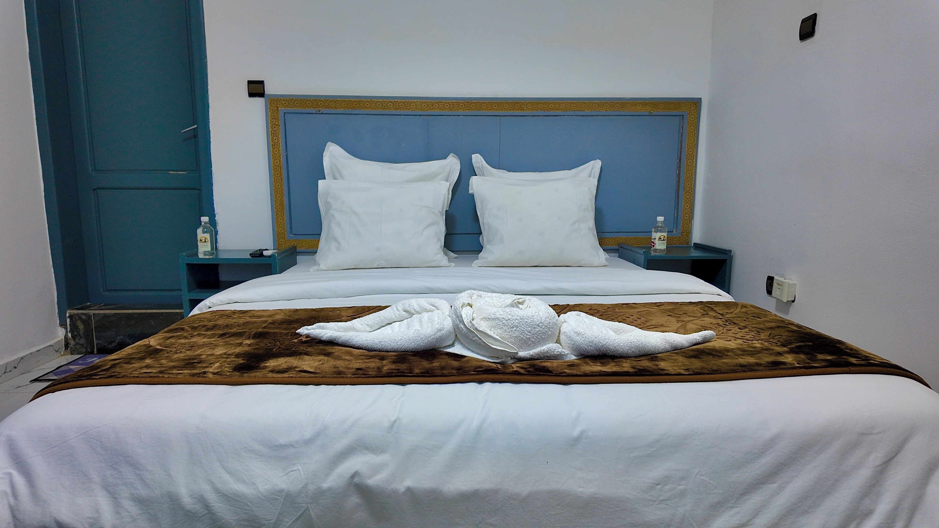 Una habitación de hotel con una cama, dos almohadas, un edredón marrón y dos toallas dispuestas sobre la cama.