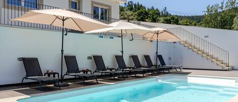 A swimming pool with lounge chairs and umbrellas, a staircase, and a building with windows.