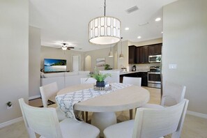 A dining area with a round table, chairs, a ceiling fan, and a kitchen in the background. - Luxury Home in Paseo Fort Myers (Fort Myers)