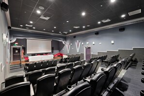 A conference room with rows of black chairs, a white projection screen, and a stage with a red table. - Luxury Home in Paseo Fort Myers (Fort Myers)