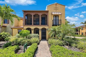 A two-story building with a central entrance, arched windows, and a balcony with a striped awning. - Luxury Home in Paseo Fort Myers (Fort Myers)