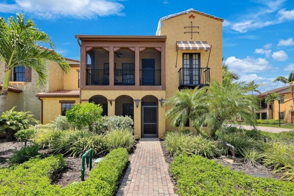 A two-story building with a central entrance, arched windows, and a balcony with a striped awning. - Luxury Home in Paseo Fort Myers (Fort Myers)