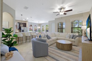 A spacious living room with a sectional sofa, a round coffee table, and a dining area with bar stools.