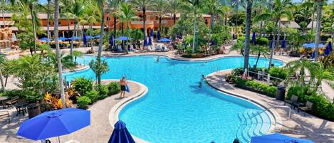 A resort pool area with multiple swimming pools, lounge chairs, and umbrellas.