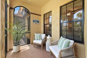 A sunlit balcony with two wicker chairs, a potted plant, and a lantern. - Luxury Home in Paseo Fort Myers (Fort Myers)
