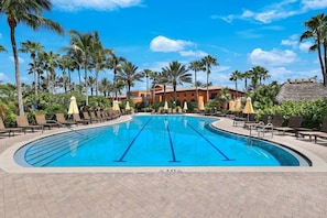 A swimming pool with lounge chairs and umbrellas, surrounded by palm trees and a building in the background. - Luxury Home in Paseo Fort Myers (Fort Myers)