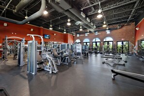 A gym with various exercise equipment, a brick wall, and large windows.