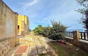 Un escalier en pierre menant à un bâtiment d’où l’on a une vue sur la mer.
