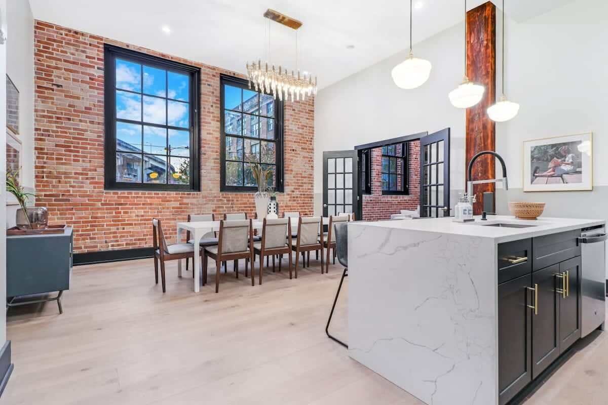 A modern kitchen with a large island, brick walls, and large windows.