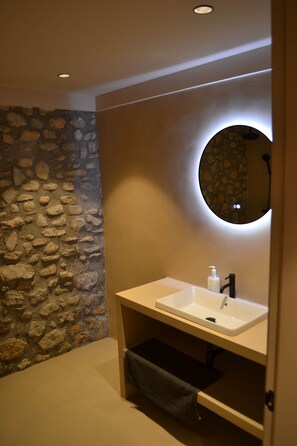 A bathroom with a stone wall, a round mirror, and a white sink. - Can Hortafa - Country House in Tortellà - Cortada de la Cellera (Tortellà)