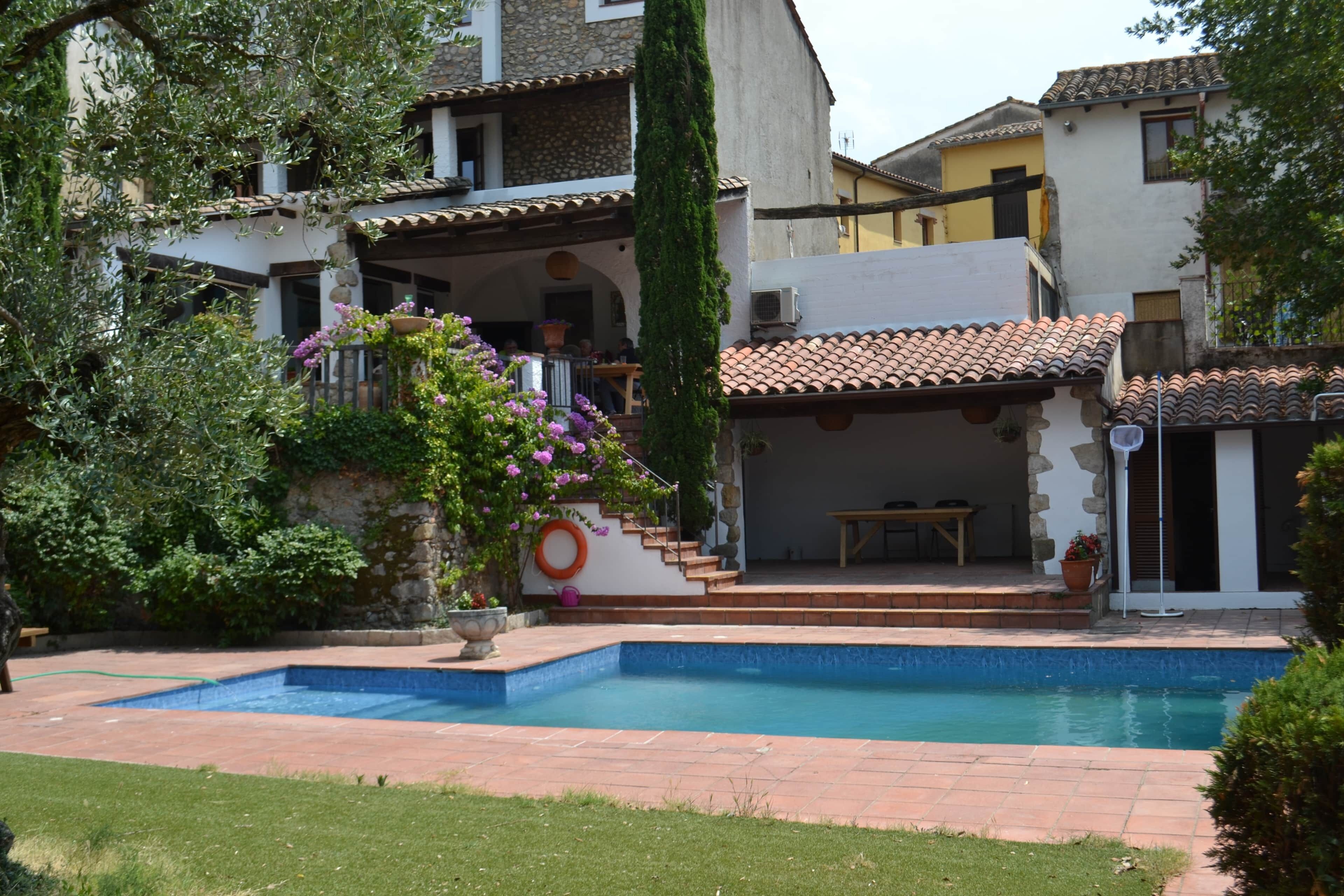 A residential property with a swimming pool, a covered patio, and a stone staircase leading to a second-floor balcony.