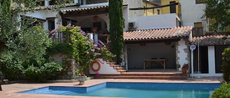 Um imóvel residencial com piscina, varanda coberta e escadaria de pedra que leva a uma varanda no segundo andar.