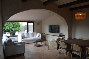 A spacious living area with a white sofa, a dining table with chairs, and a TV mounted on the wall. - Can Hortafa - Country House in Tortellà - Cortada de la Cellera (Tortellà)