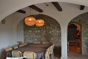 A dining area with a stone wall, a table with chairs, and two hanging light fixtures. - Can Hortafa - Country House in Tortellà - Cortada de la Cellera (Tortellà)
