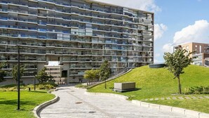 A multi-story residential building with balconies, a landscaped courtyard, and a small hill with trees. - Mall of Tripla apartments by Come in (Helsinki)