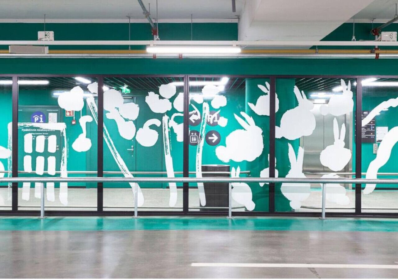 A modern indoor space with a green wall featuring white abstract art, a glass partition, and a metal railing.