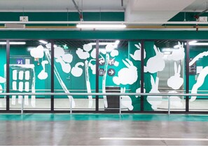 Espaço interior moderno com parede verde, arte abstrata branca, divisória de vidro e guarda-corpo metálico.