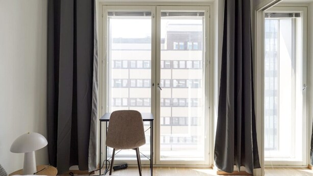 A room with a large window, a chair, and a table. - Mall of Tripla apartments by Come in (Helsinki)