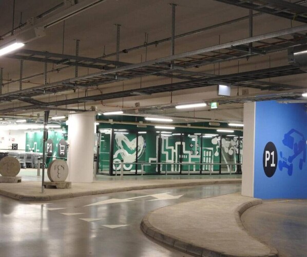 An indoor parking area with clear directional arrows on the floor, a blue pillar with 'P1' signage, and green walls with white patterns.