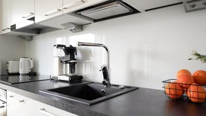 A modern kitchen with a black sink, a coffee machine, and a fruit basket. - Mall of Tripla apartments by Come in (Helsinki)