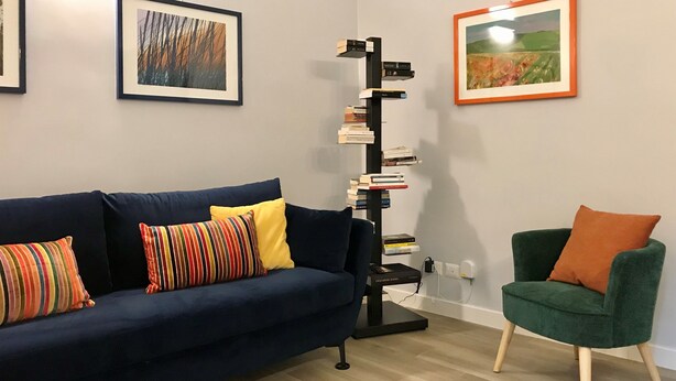 Uma sala de estar com um sofá azul escuro, uma almofada listrada, uma poltrona verde e uma estante contra a parede.