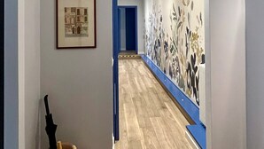 Um corredor com piso de madeira, um quadro emoldurado à esquerda e uma porta azul no final.