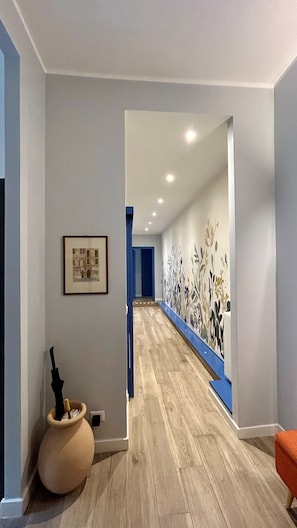 A hallway with a wooden floor, a framed picture on the left, and a blue door at the end. - St.Peter's Basilica Apartment (Roma)