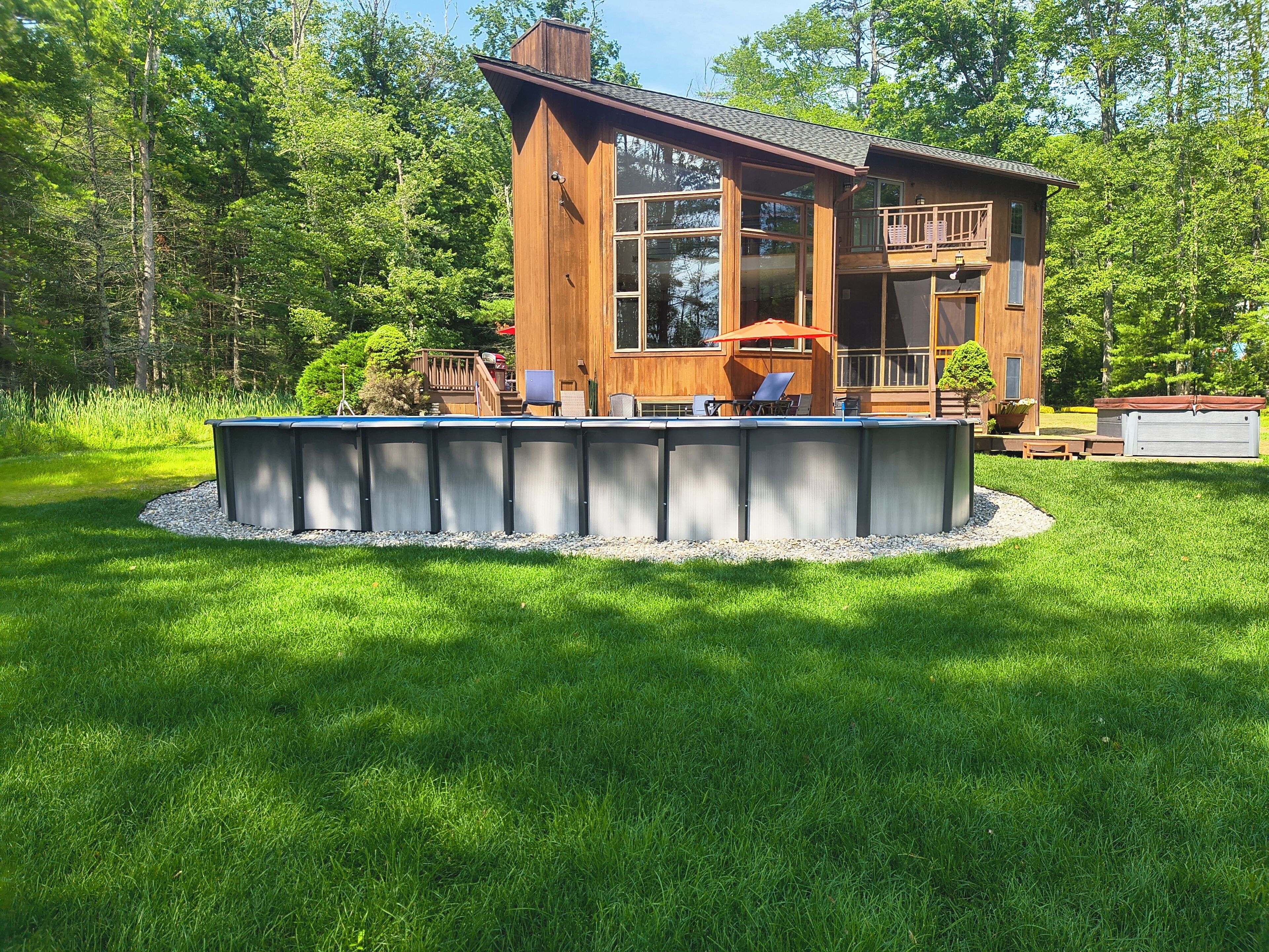 A wooden cabin with a deck, surrounded by a well-maintained lawn and trees.